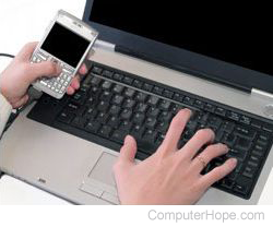 Person holding a smartphone and using a laptop.